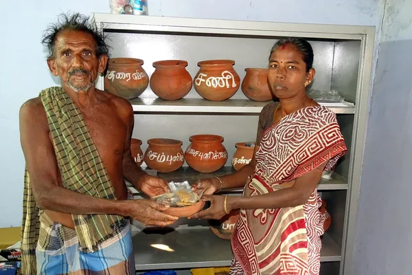 Two adults holding seed packets in front of shelves of clay storage pots.